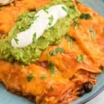 Chicken enchiladas garnished with guacamole and sour cream on a plate.