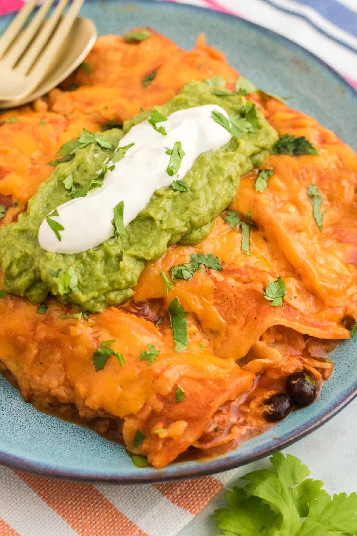 Chicken enchiladas garnished with guacamole and sour cream on a plate.