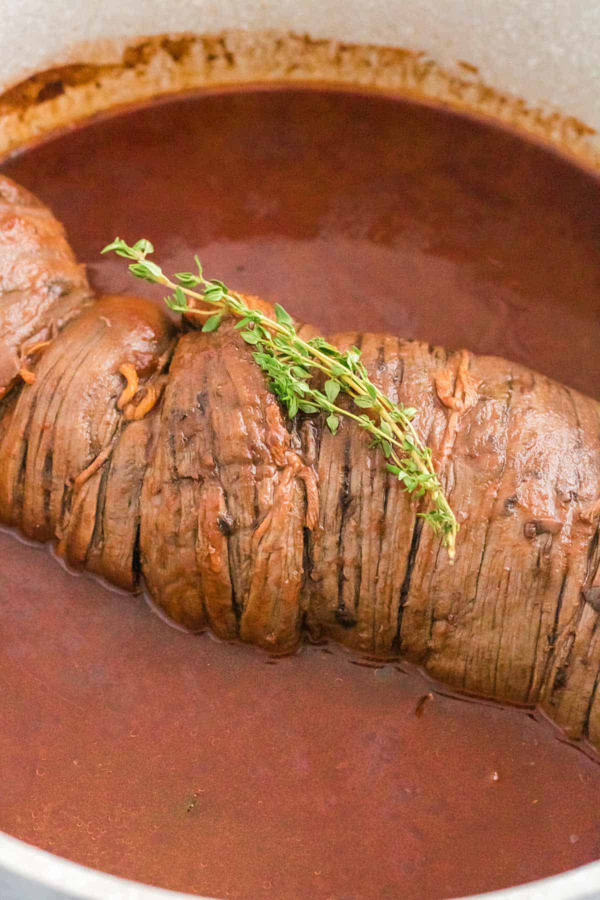 Braised beef braciole topped with thyme sprigs in a pot of red wine tomato gravy.