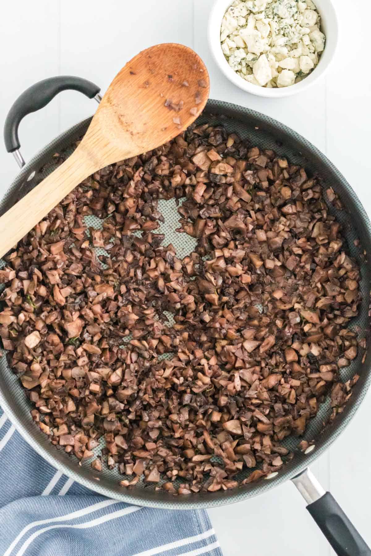 Sauteed mushroom duxelles in a skillet with a wooden spoon.