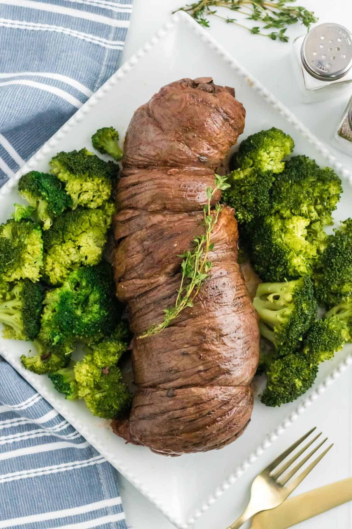 Top view of braised mushroom stuffed beef braciole on a plate next to cooked broccoli.