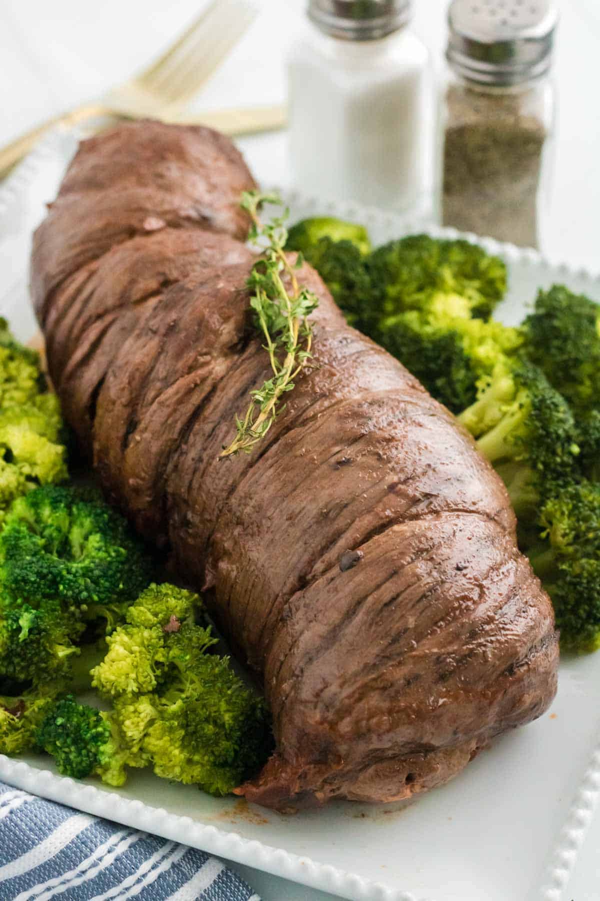 Braised mushroom stuffed beef braciole on a plate next to cooked broccoli.