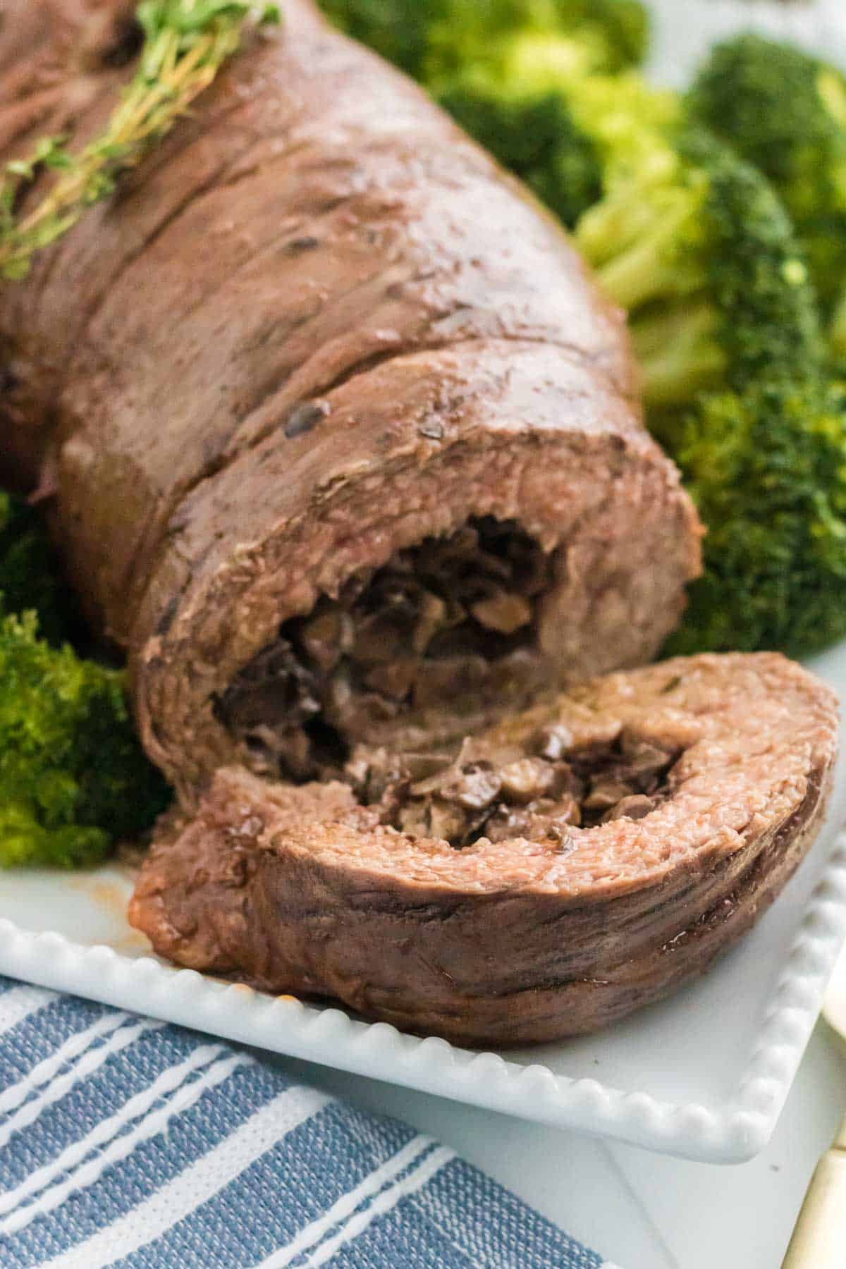 Sliced mushroom stuffed beef braciole on a plate next to cooked broccoli.