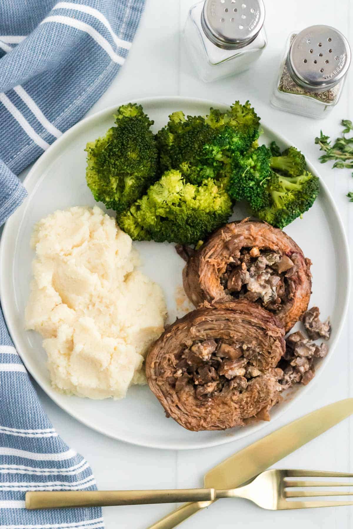 Stuffed flank steak pinwheels served on a plate with broccoli and mashed potatoes.
