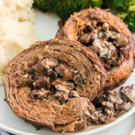 Mushroom stuffed Beef Wellington braciole pinwheels on a plate with broccoli and mashed potatoes.