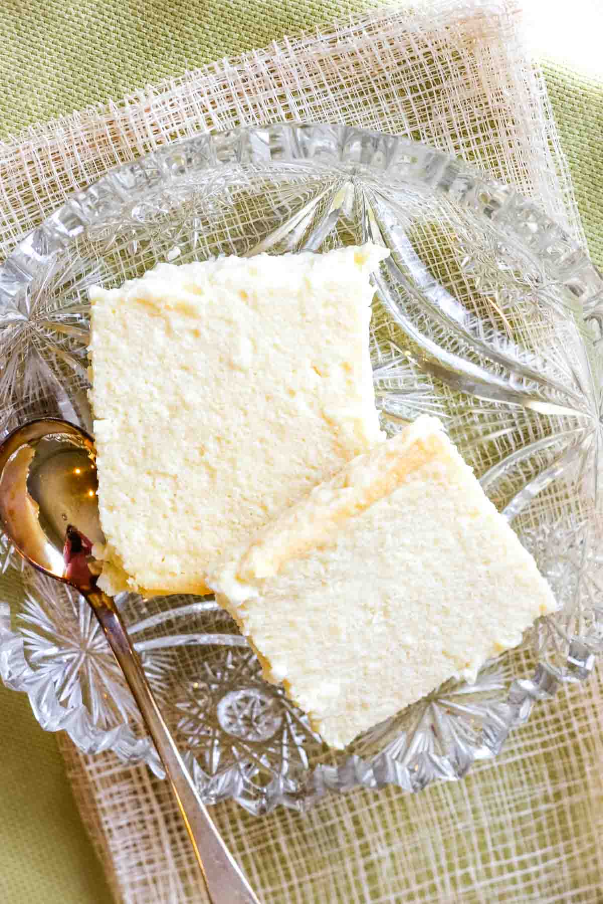 An overhead view of two squares of Ukrainian cheesecake in a crystal dish with a silver spoon.