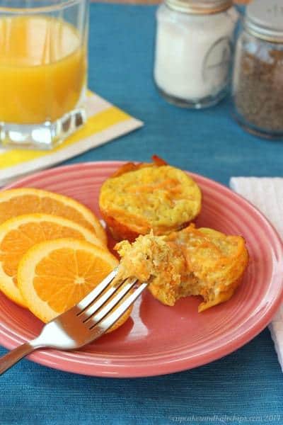 Cheesy apple sweet potato egg muffin cups on a pink plate next to orange slices.