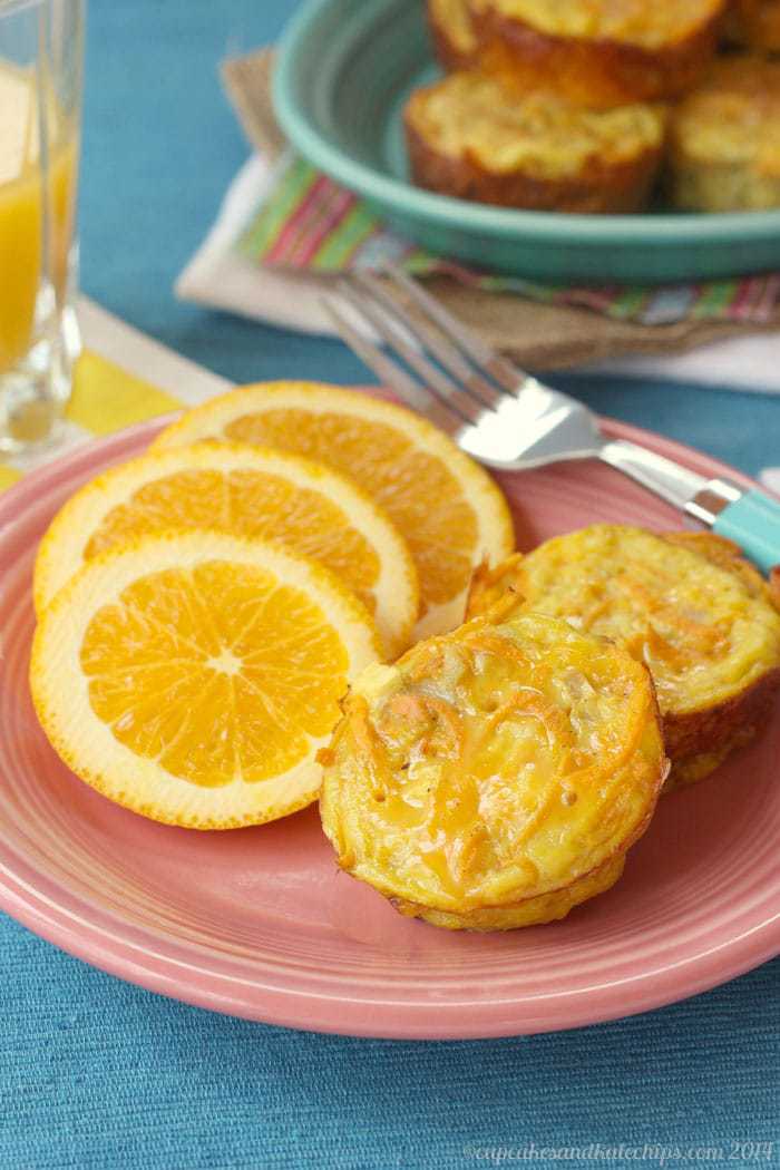 Cheesy apple sweet potato egg muffin cups on a pink plate next to orange slices.