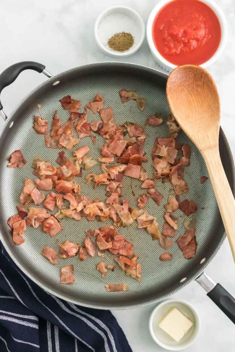 Bacon pieces cooked in a skillet next to a wooden spoon.