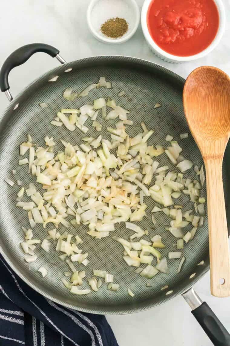 Cooked onions in a skillet next to a wooden spoon.