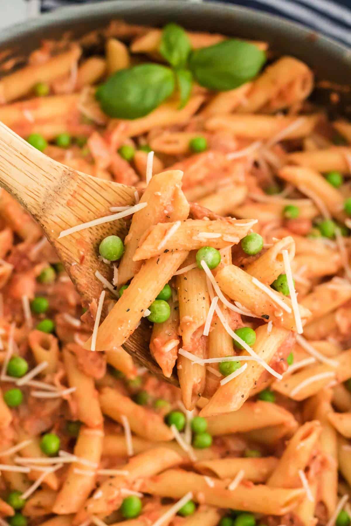 Close up of a spoonful of penne with tomato cream sauce, with a pan of pasta in the background.