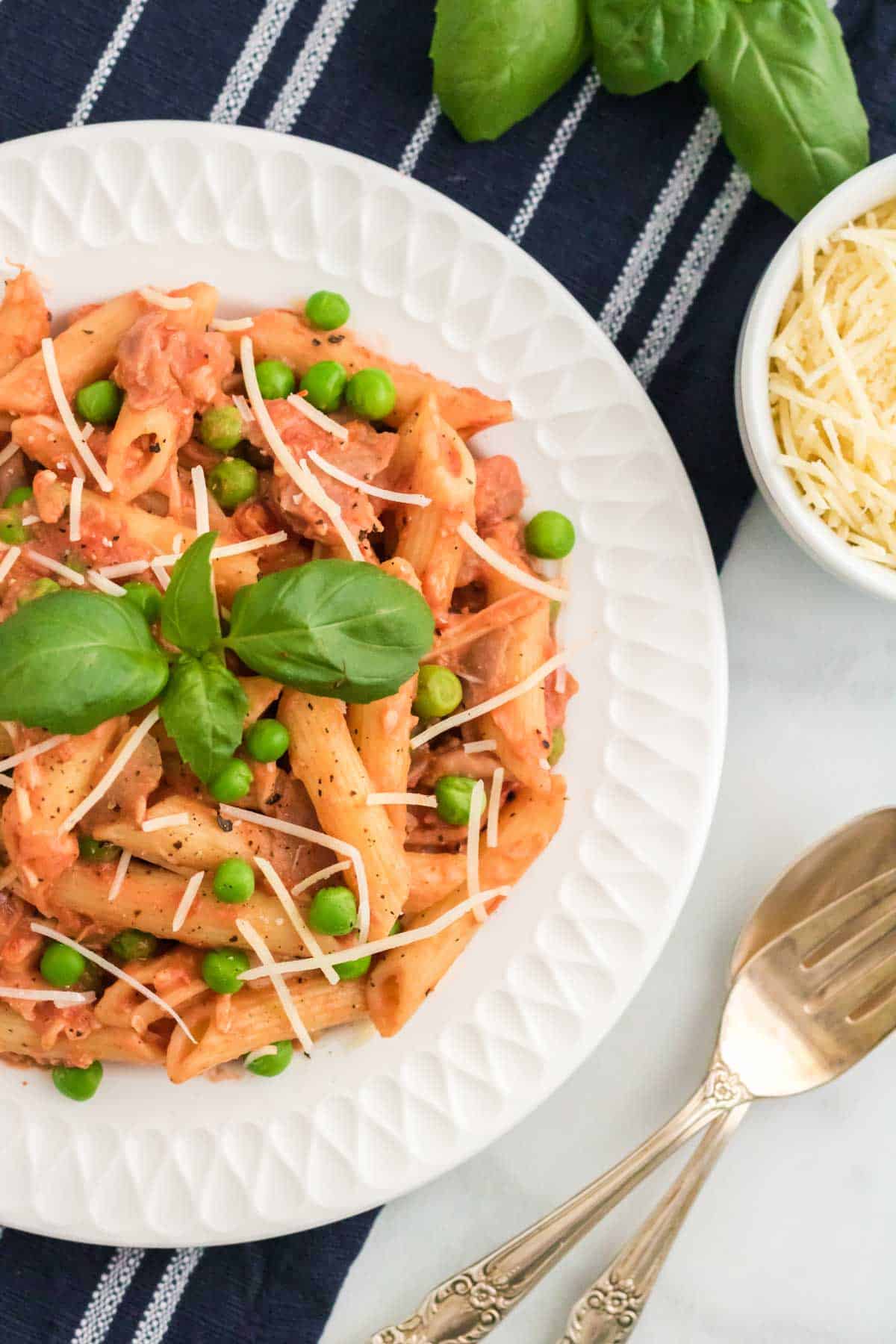 Penne with tomato cream sauce on a plate topped with peas and prosciutto.