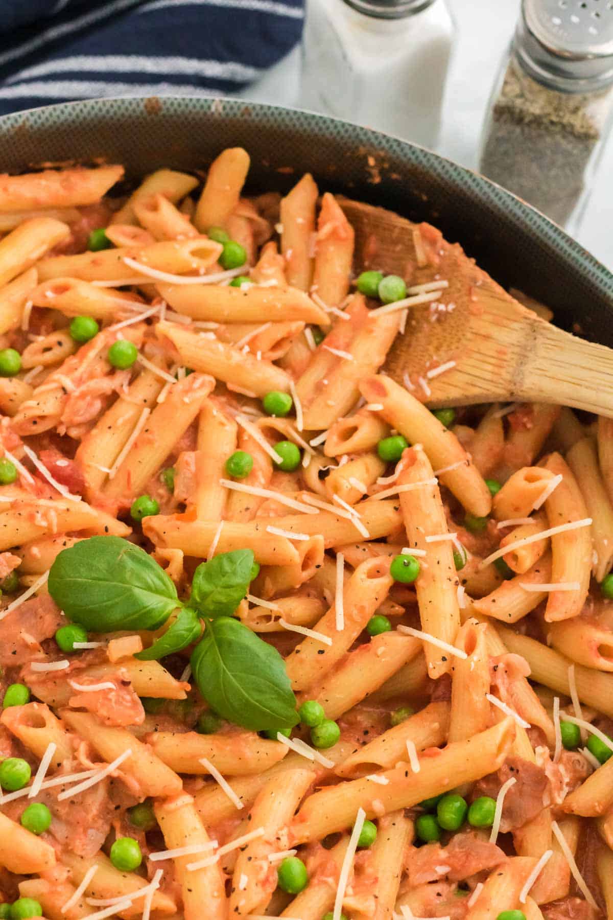 A pan of penne with tomato cream sauce, with a wooden spoon.
