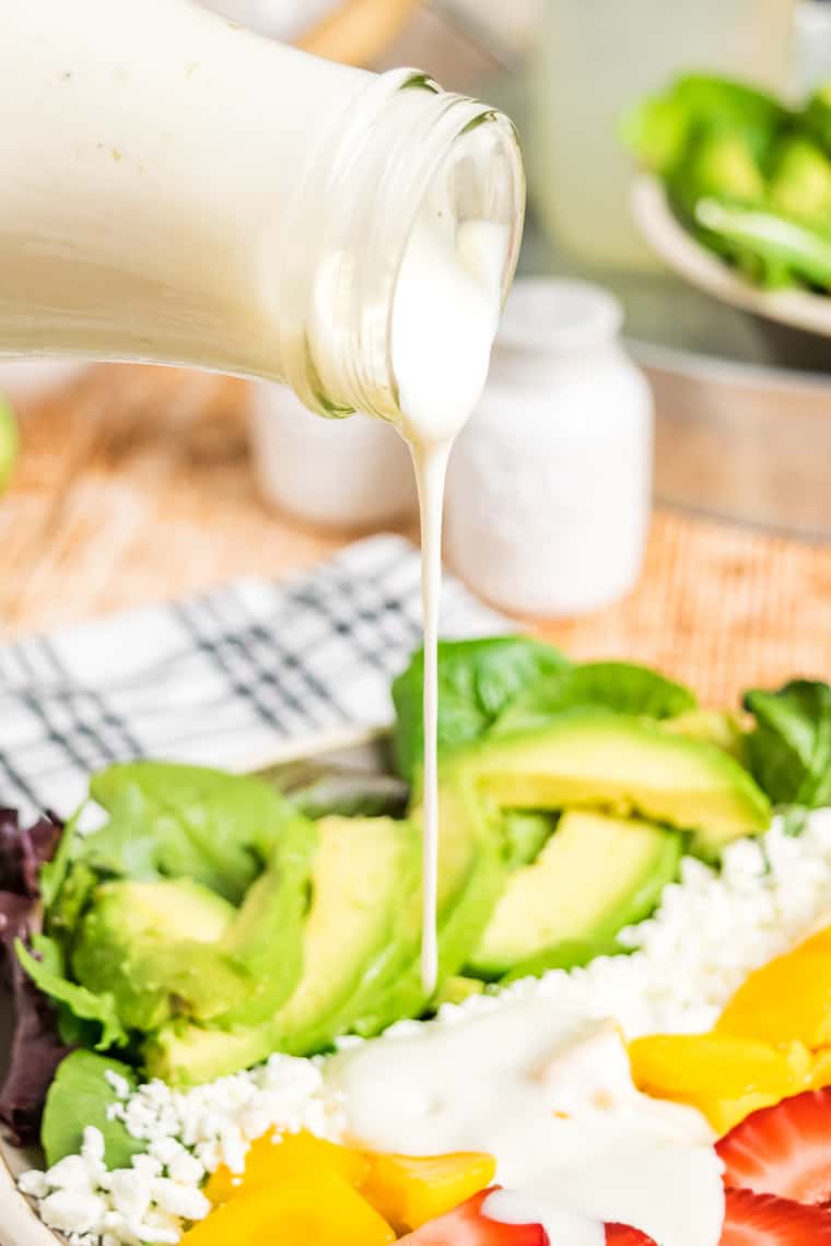 Pouring the dressing over a salad with fruit, cheese, and avocado