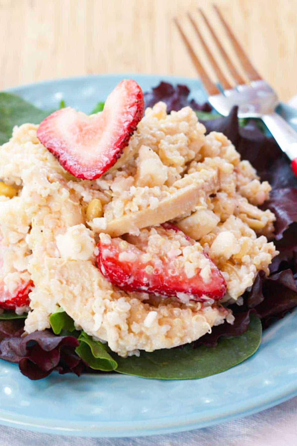 A closeup of a scoop of quinoa chicken salad with strawberry slices.