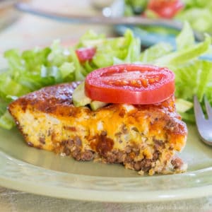 A piece of bacon cheeseburger crustless quiche on a green plate topped with a slice of tomato.