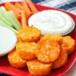 Spicy cauliflower tots on a red plate with bowls of ranch and blue cheese dressing and raw carrots and celery.
