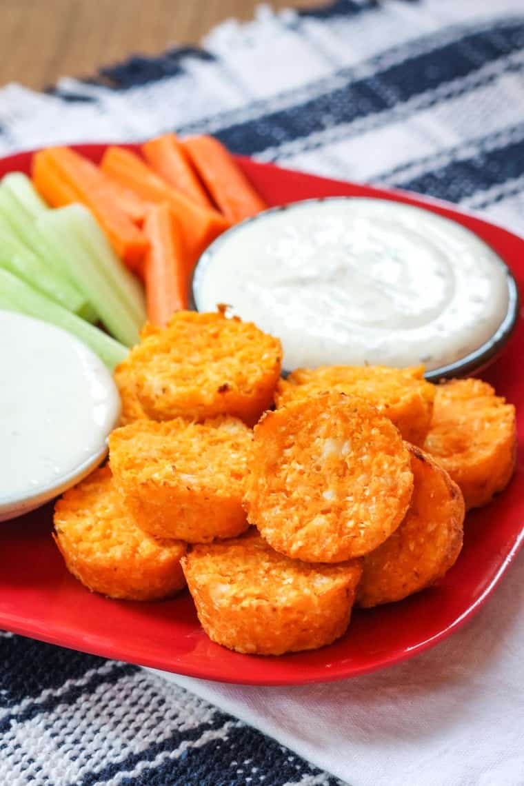 Spicy cauliflower tots on a red plate with bowls of ranch and blue cheese dressing and raw carrots and celer