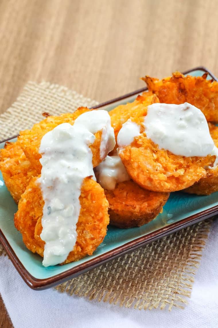 Buffalo cauli tots on a turquoise plate with blue cheese dressing dripping over them