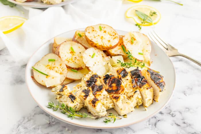 Slice lemon chicken breast on a white plate with potatoes