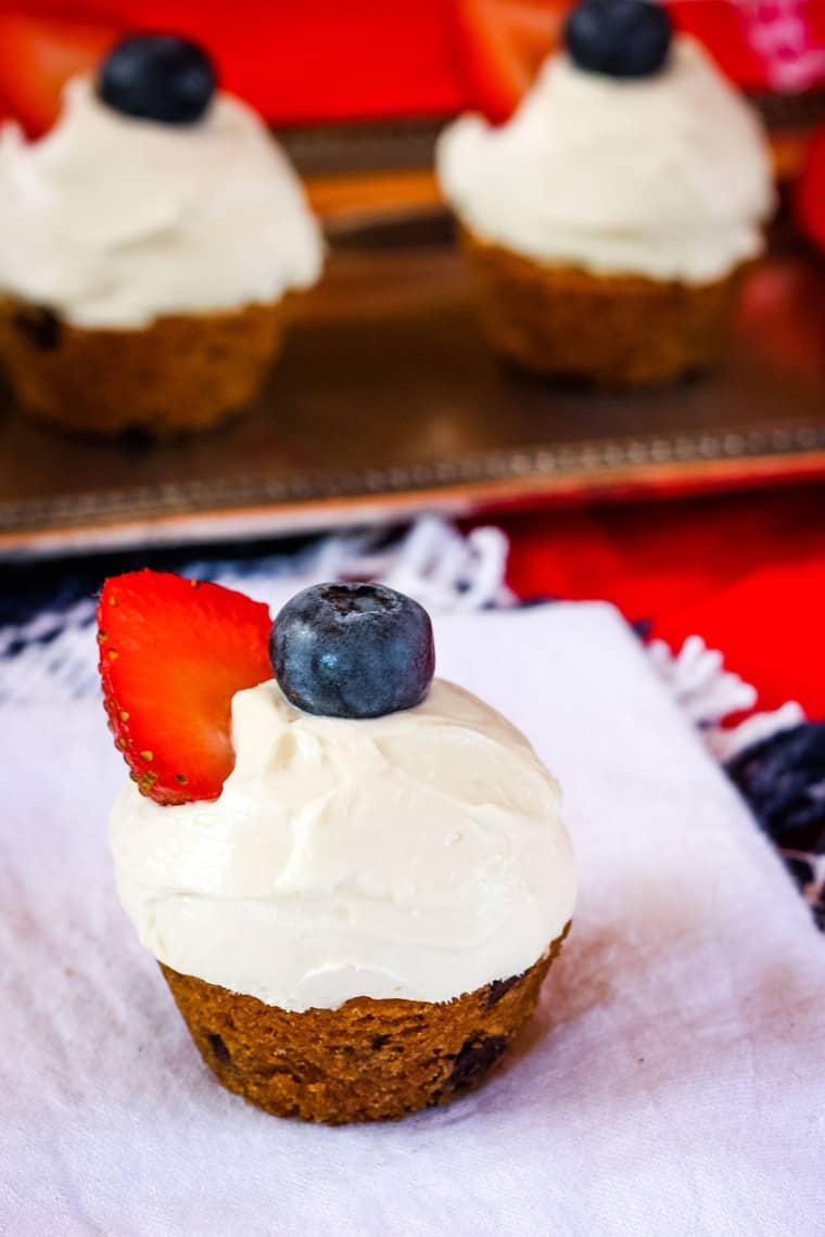 Mini Chocolate Chip Cookie Cup with Cream cheese frosting, a blueberry, and a strawberry slice on a white napkin