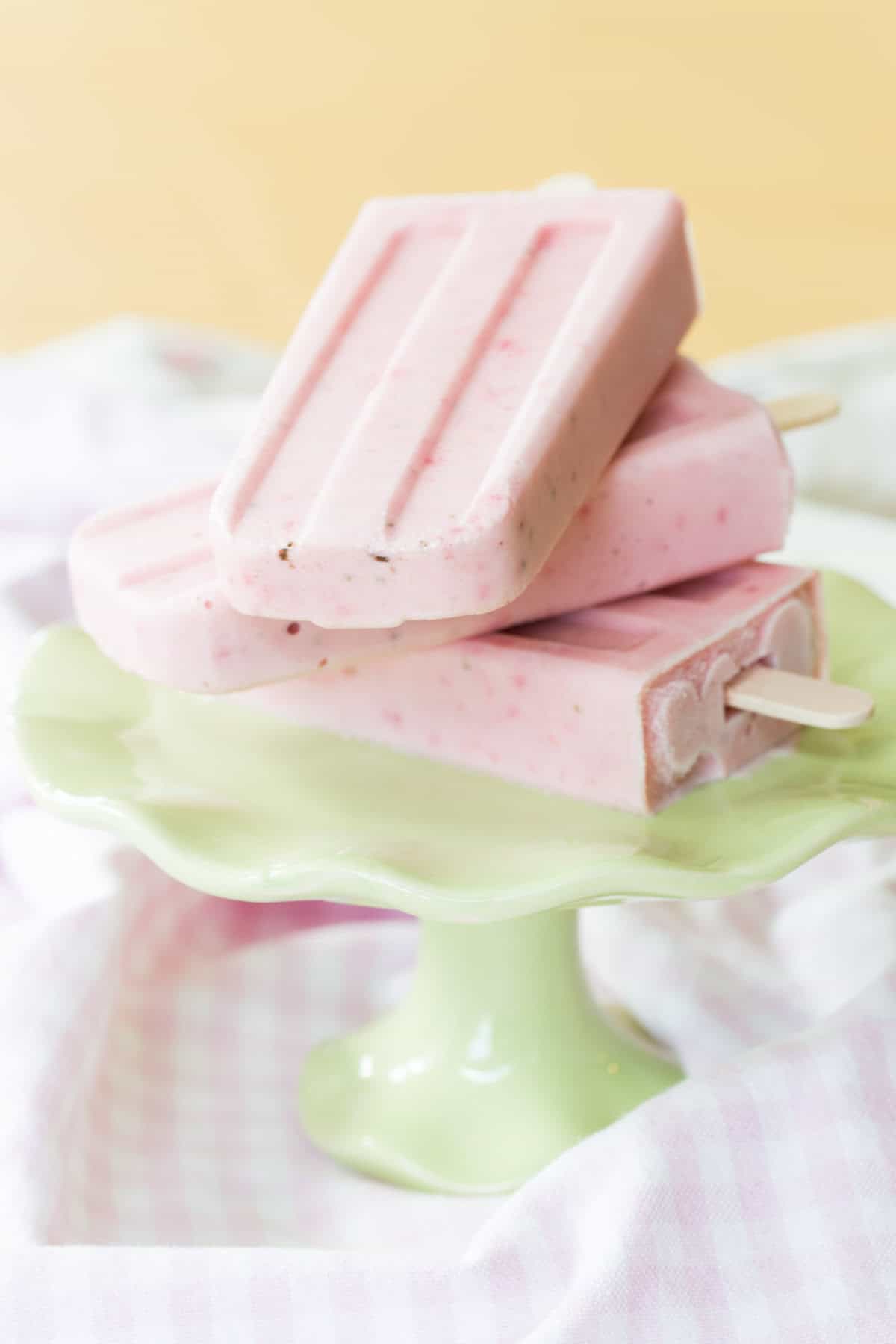 Three Strawberry Cheesecake Frozen Yogurt Popsicles stacked on a green platter