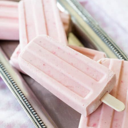 Several strawberry yogurt popsicles scattered on a pewter platter.