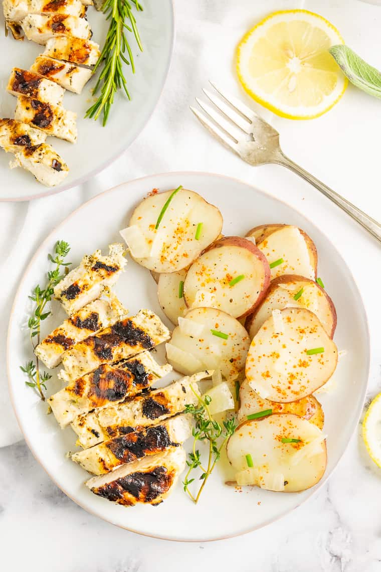 Grilled chicken dinner on a plate with cooked potato slices