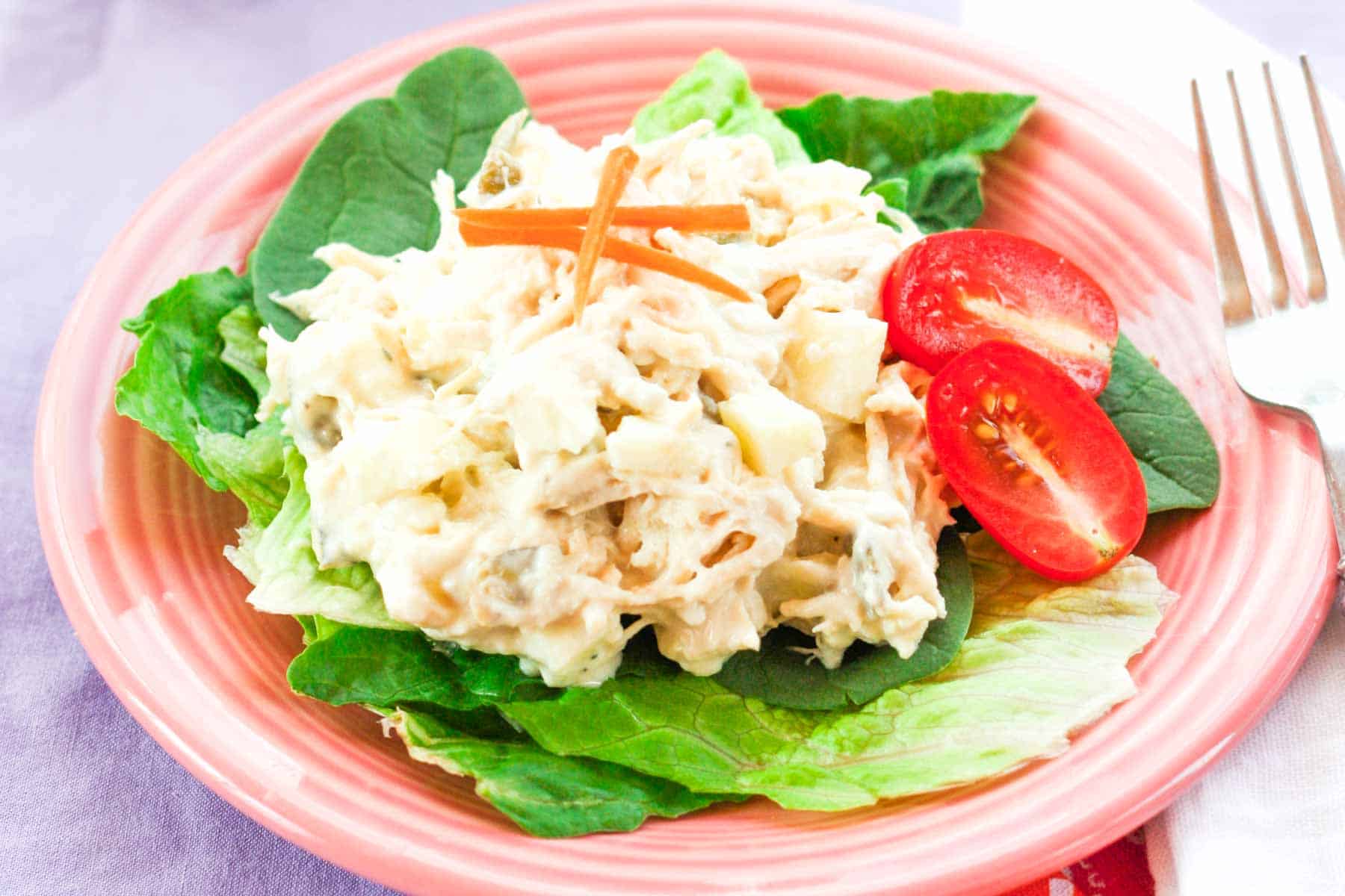 Apple chicken salad on top of a bed of lettuce on a pink plate.