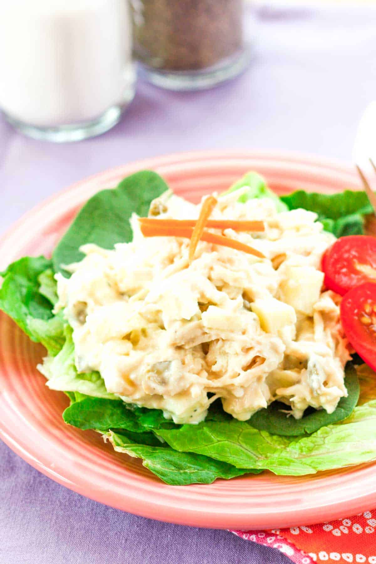 Chicken salad with apples on top of lettuce leaves on a pink plate.