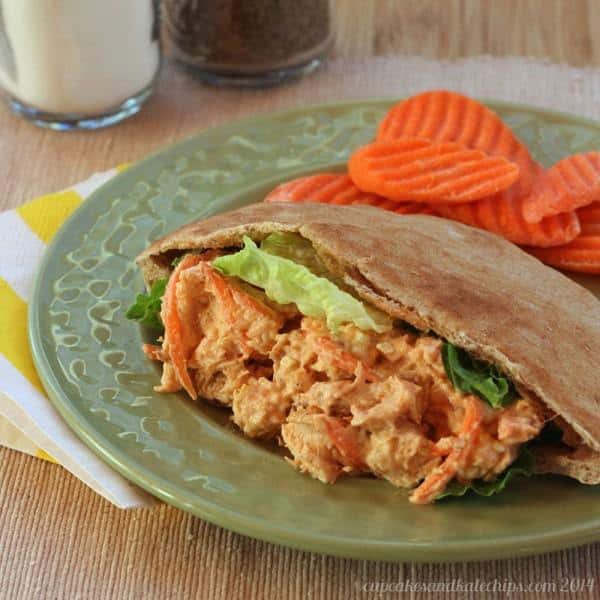 Buffalo chicken salad in a pita wrap, on a green plate with carrot slices.