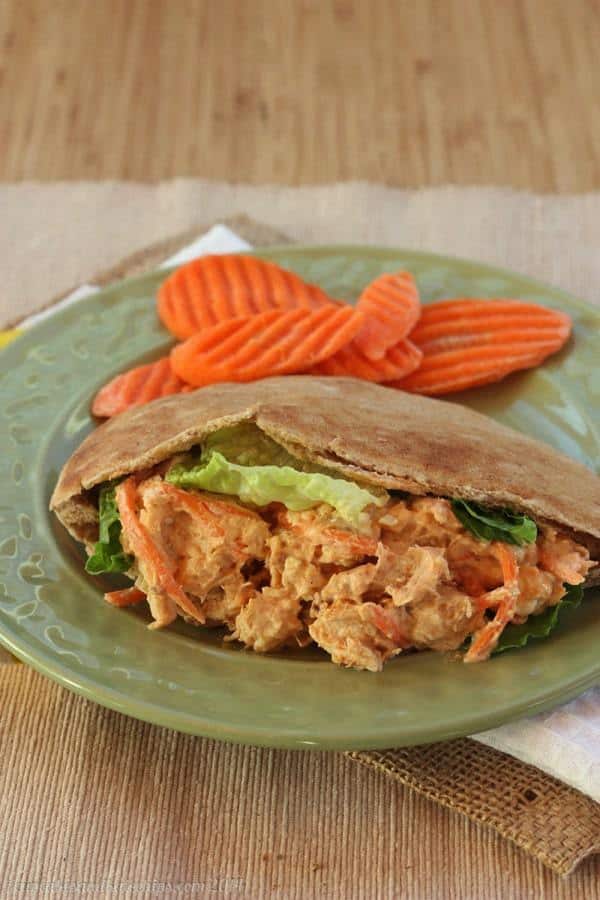 Buffalo chicken salad in a pita wrap, on a green plate with carrot slices.