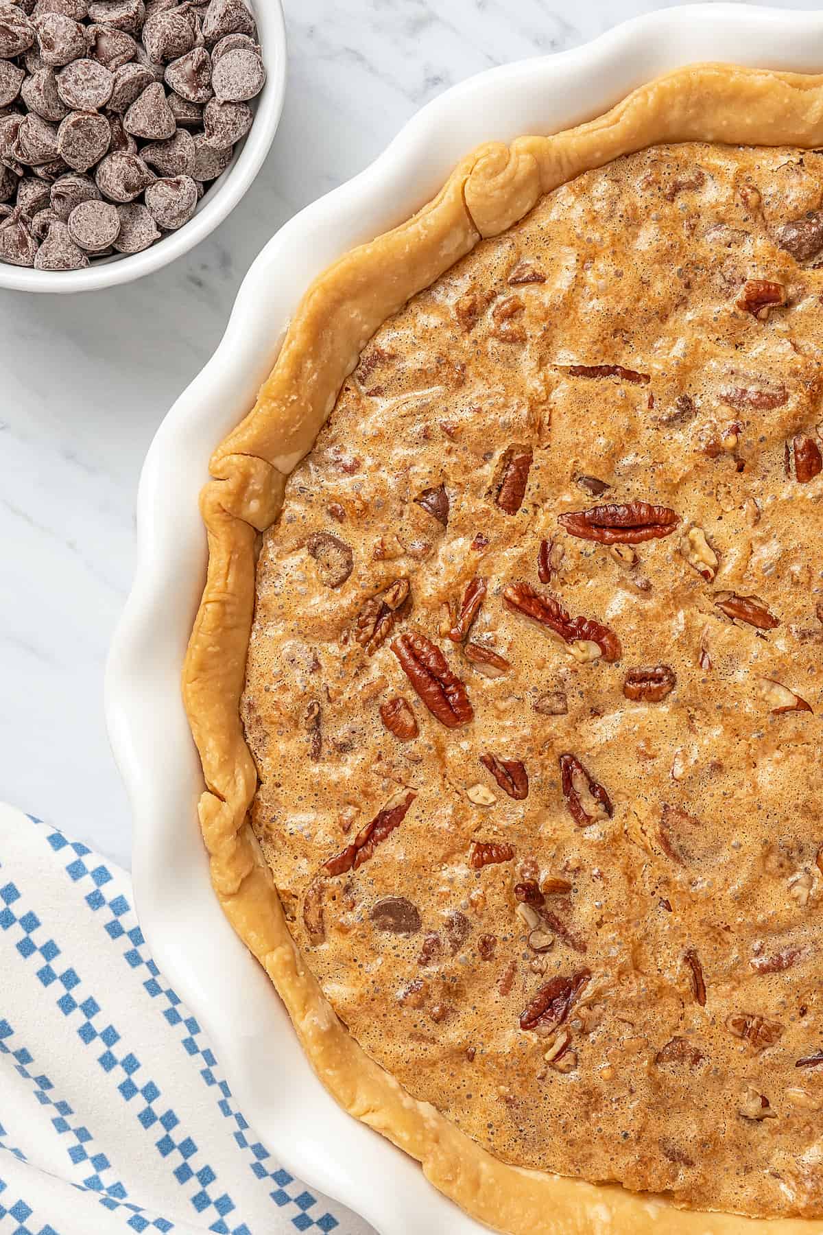 Close up of a baked chocolate chip cookie pie next to a small bowl of chocolate chips.