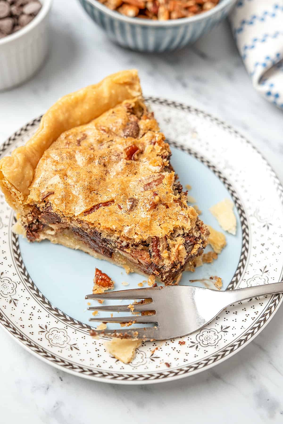 A slice of gluten free chocolate chip cookie pie on a china plate with a fork and a bite already taken from it.