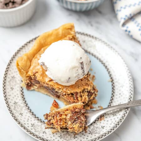 A slice of gluten-free chocolate chip cookie pie on a plate, topped with chocolate chip vanilla ice cream, with a forkful missing.