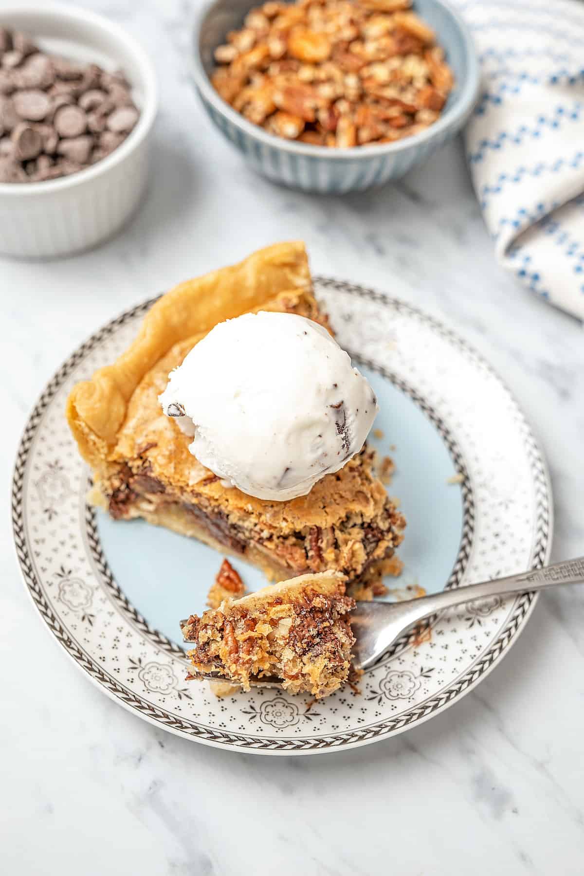 A slice of gluten-free chocolate chip cookie pie on a plate, topped with chocolate chip vanilla ice cream, with a forkful missing.