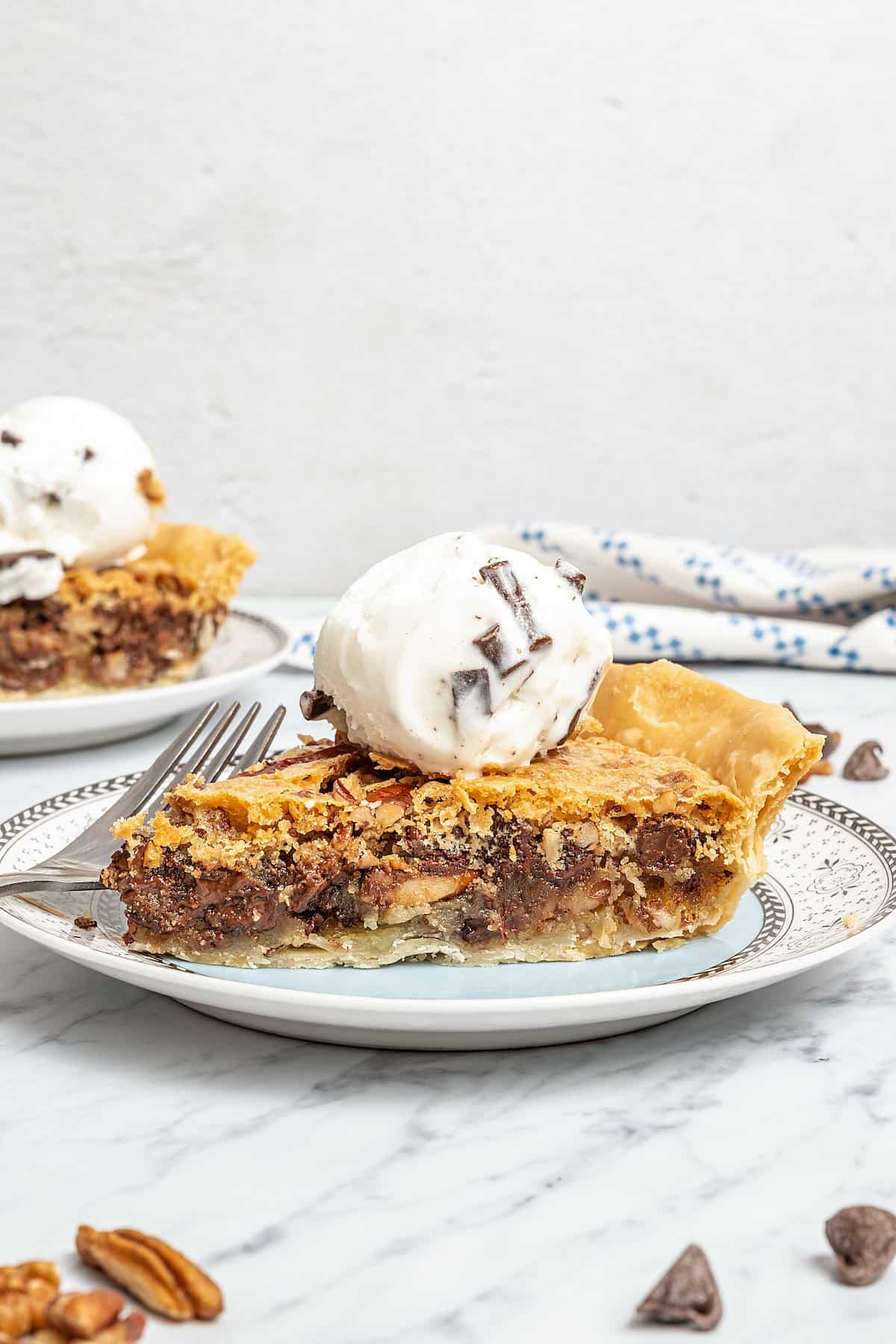 A slice of gluten-free chocolate chip cookie pie on a plate, topped with chocolate chip vanilla ice cream.