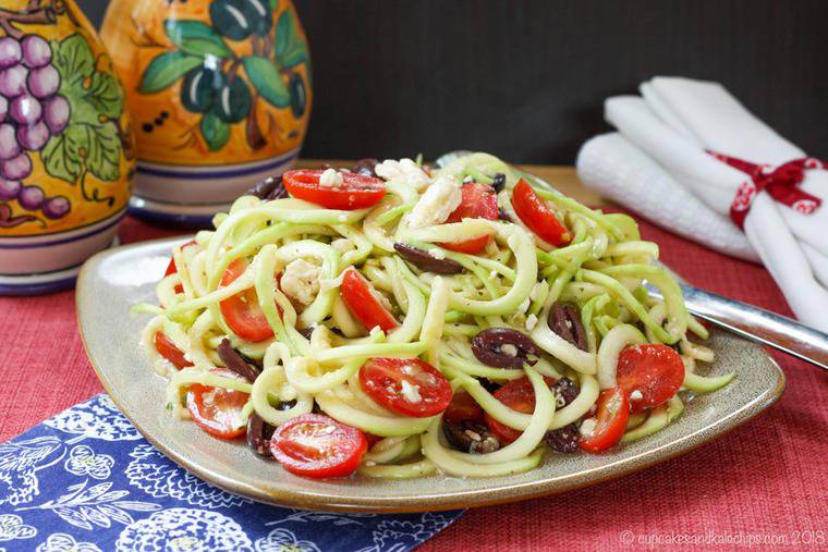 Zucchini Noodle Greek Salad on a plate with oil and vinegar bottles in the background