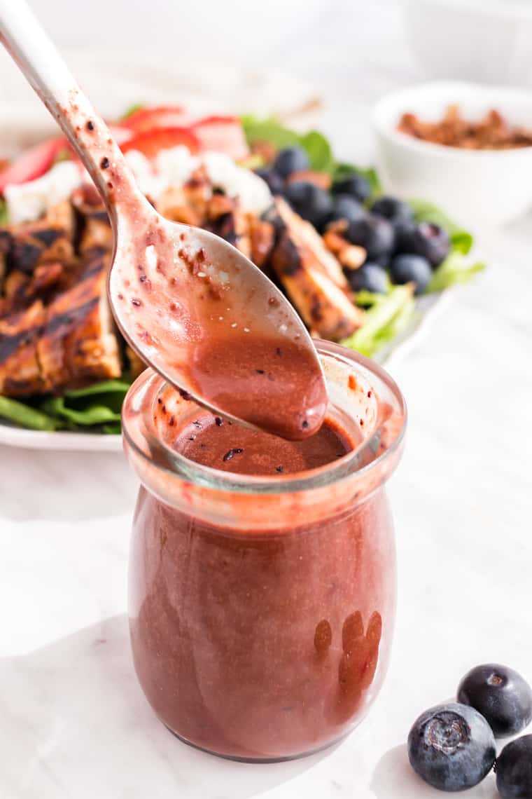 A spoon with Maple Balsamic Blueberry Vinaigrette dripping into a jar