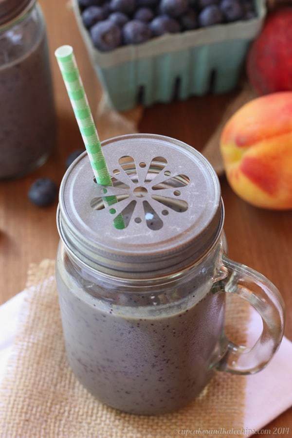 A Blueberry and Peach Green Smoothie in a sipping cup with a straw.