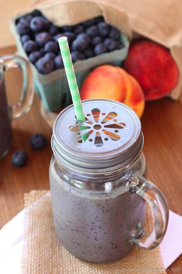 A Blueberry and Peach Green Smoothie in a sipping cup with a straw.