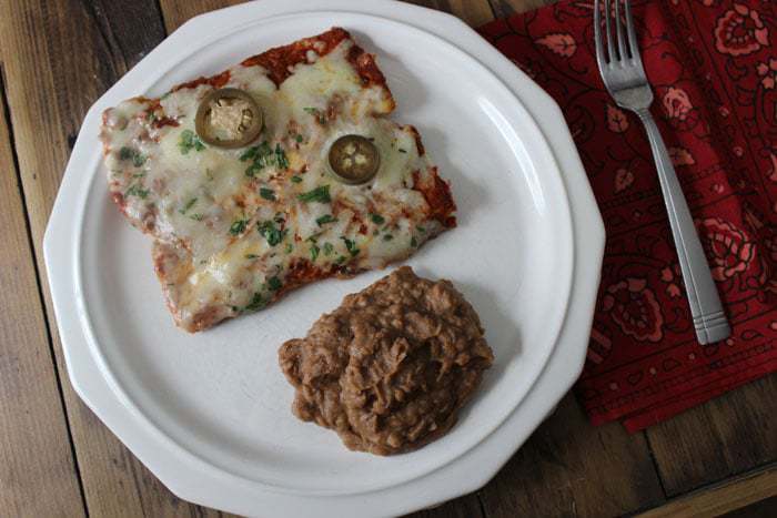 A breakfast enchilada on a plate next to refried beans.