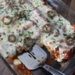 Cheesy breakfast enchiladas are scooped from a casserole dish with a spatula.