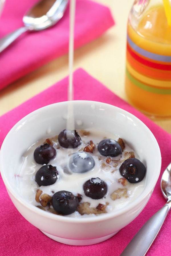 Pouring milk on a bowl of reheated freezer oatmeal cups with blueberries