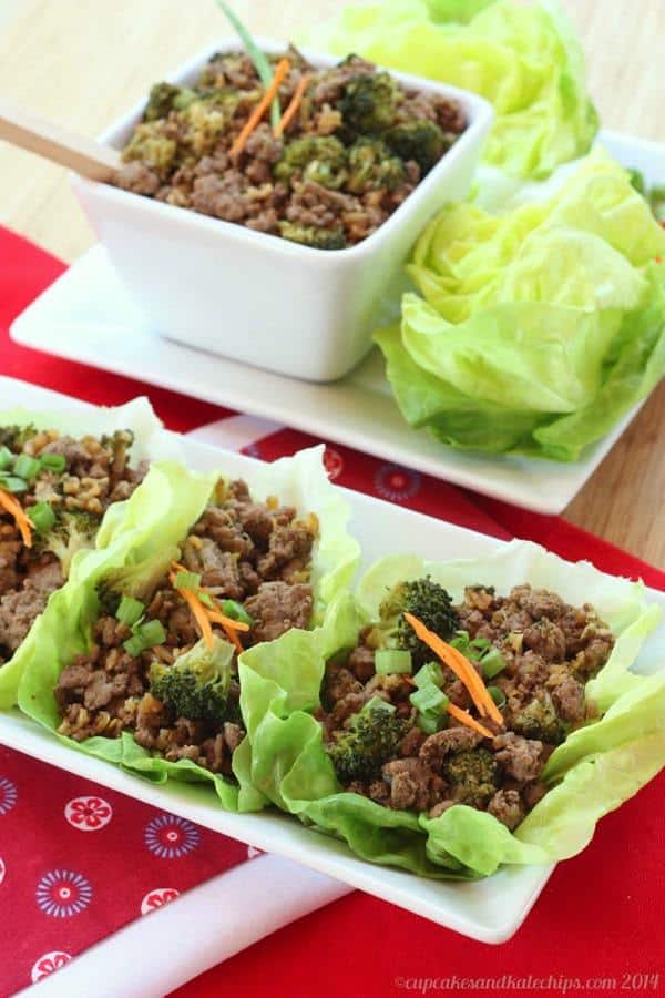 Three Asian beef and broccoli lettuce wraps on a rectangular plate with the beef filling and additional lettuce leaves in the background.