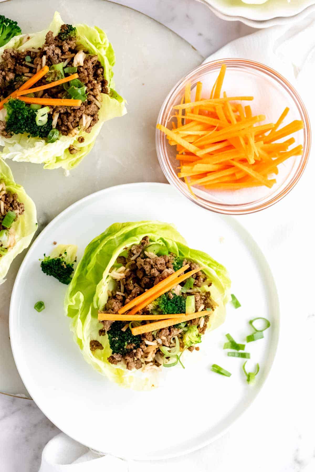 Overhead view of an Asian lettuce wrap on a plate next to a bowl of julienne carrots.