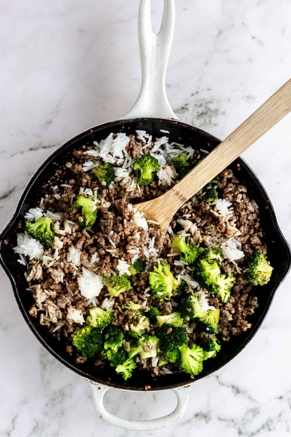 Asian beef combined with broccoli and rice in a skillet with a wooden spoon.