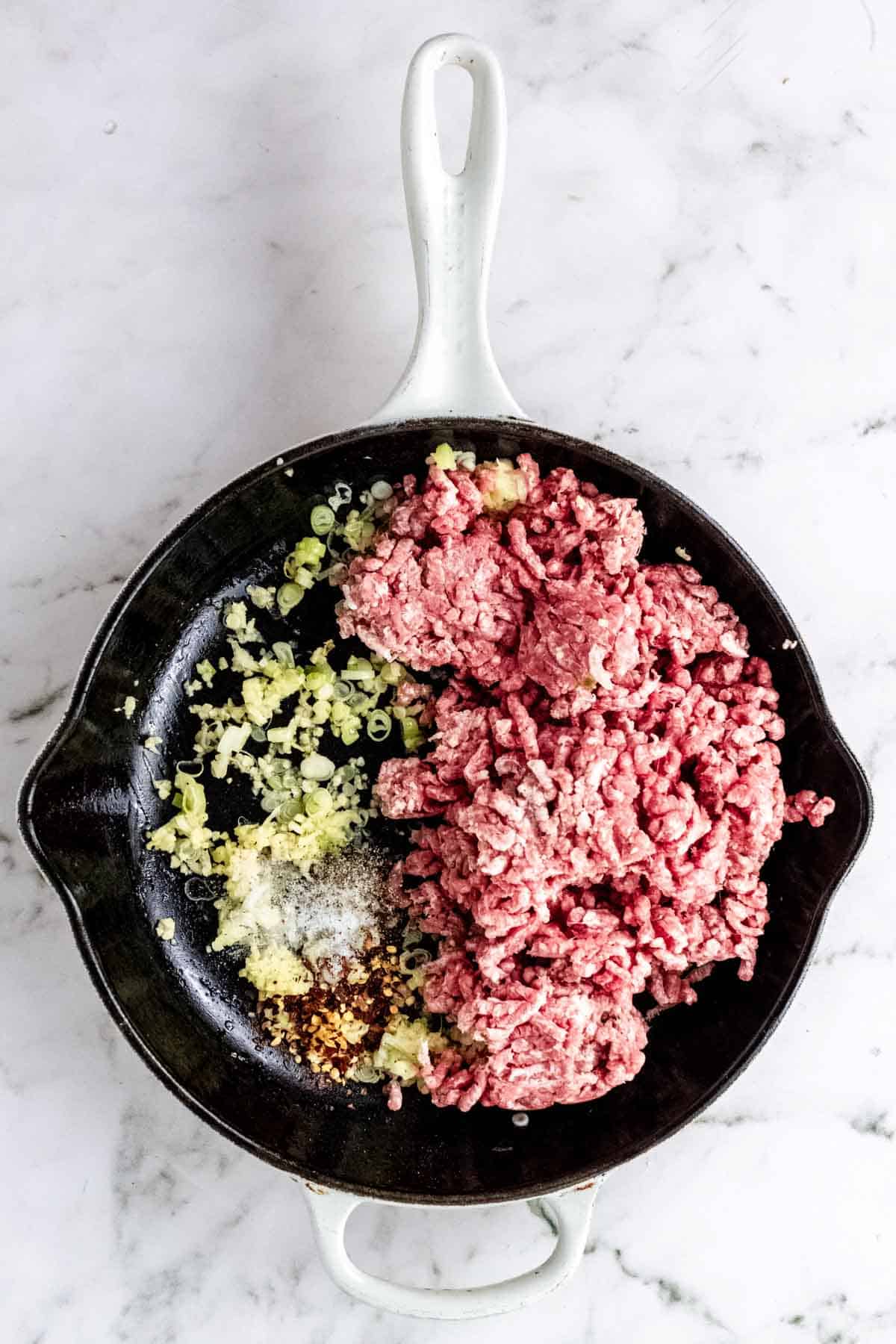 Ground beef is added to a skillet with sauted scallions.
