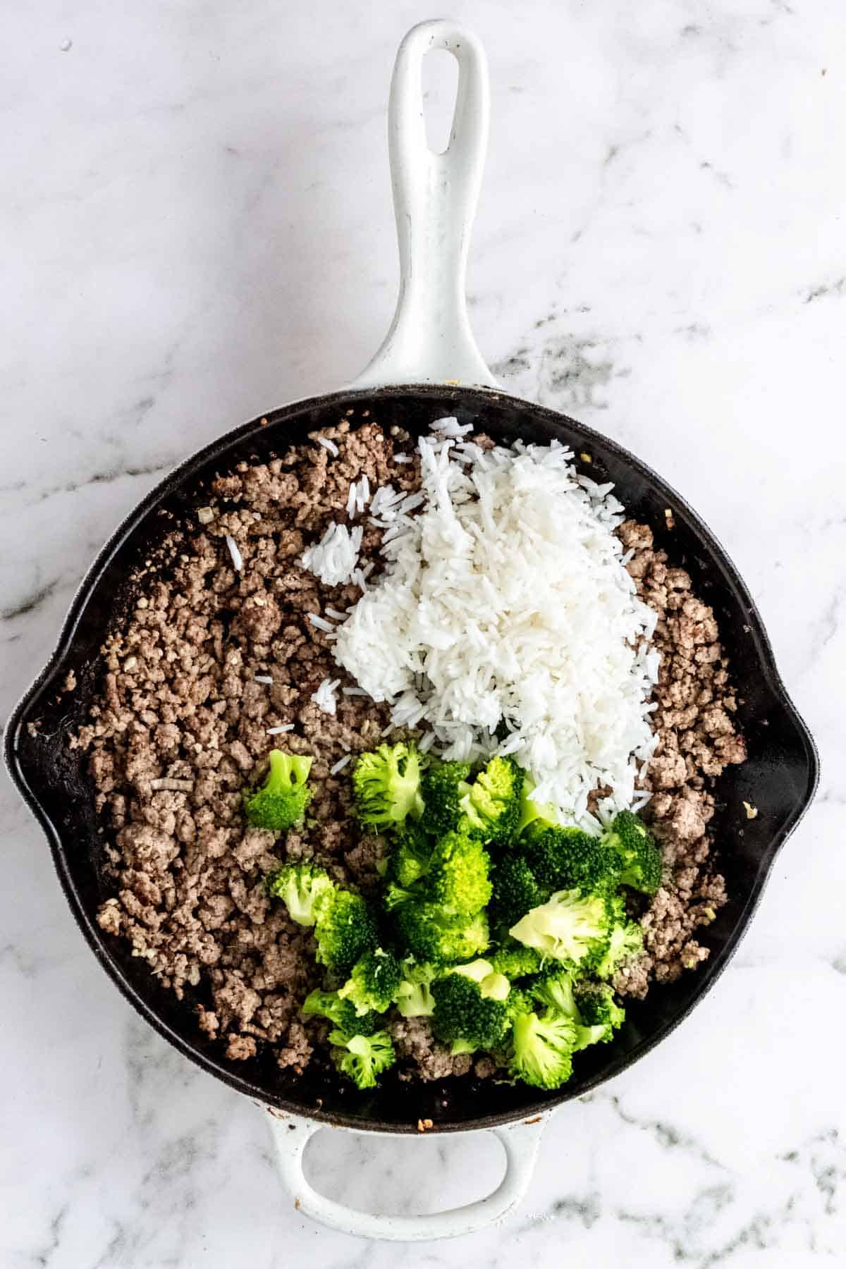 Cooked rice and broccoli added to a skillet with ground beef.