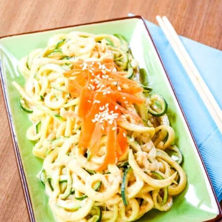 Sesame Peanut Zucchini Noodles on a green plate with wooden chopsticks on a blue napkin on the side.